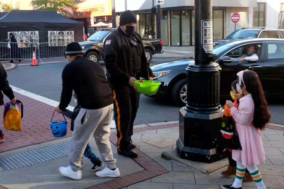 Children in Halloween costumes at a crosswalk with officer offering bowl of candy